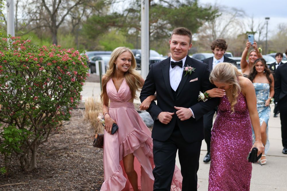 Formal attendees in elegant dresses and tuxedos walk together outside during a special event.