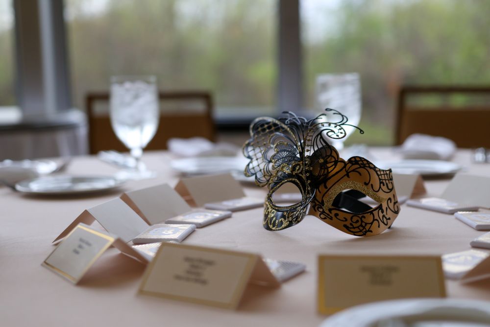 An elegant masquerade mask sits on a formal table setting with place cards and wine glasses.