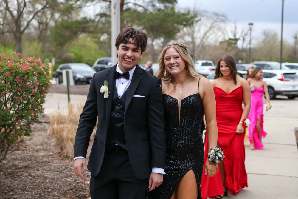 A couple walks together on a path while dressed in formal attire for a special occasion.