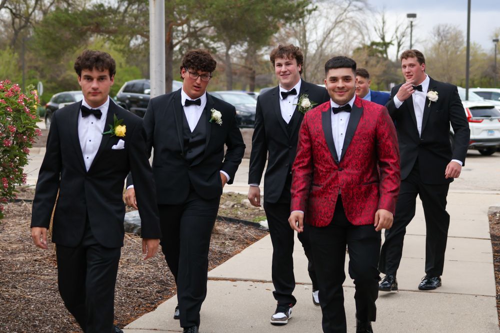 A group of young men in tuxedos walk together, with one wearing a striking red jacket.