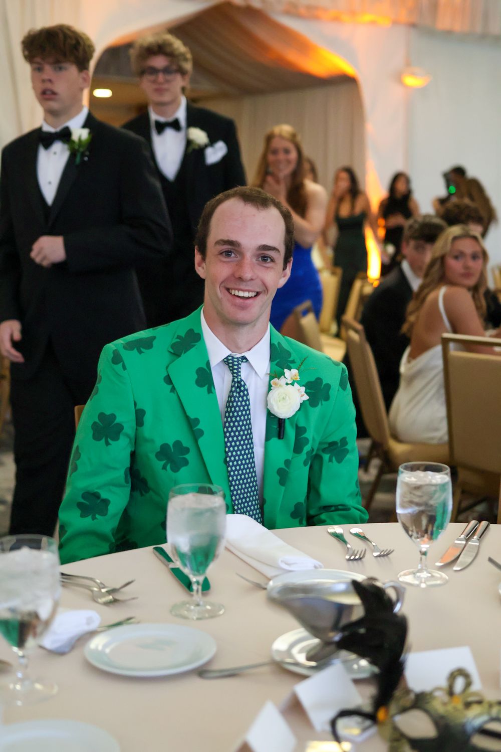 A guest in a festive green shamrock jacket sits at a formal table setting.