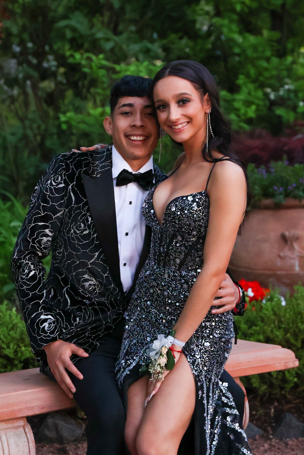 A couple in formal attire poses together in a garden setting during prom night.