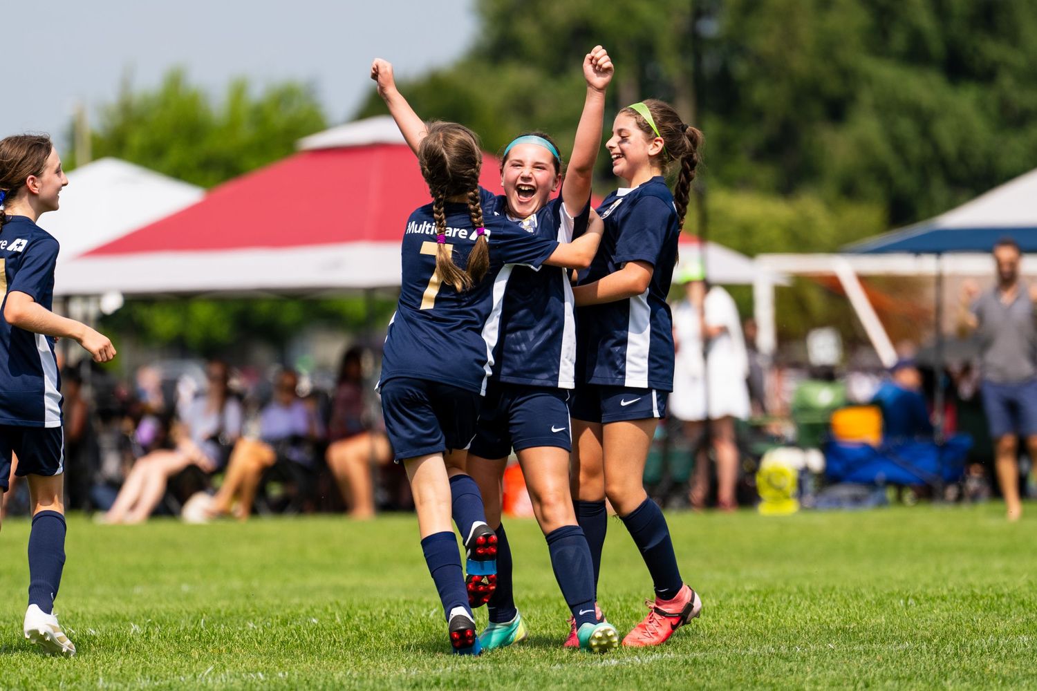 A young female soccer player from Reign Academy celebrates scoring a goal with her teammates, raising her arms.
