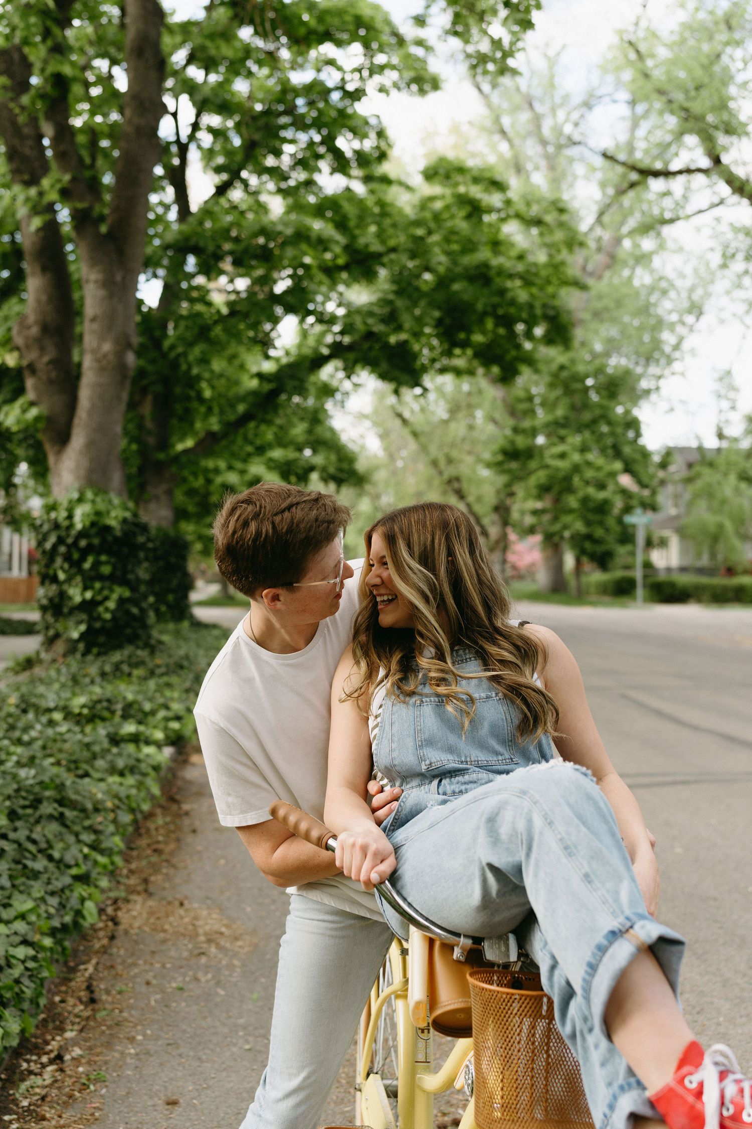 Couple sharing a playful moment on a yellow bicycle on a tree-lined street.