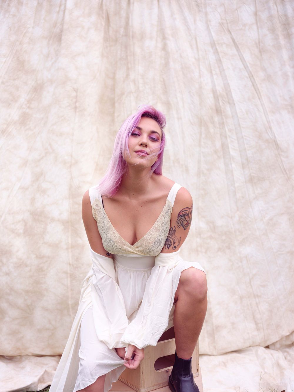 Portrait in white dress and combat boots against textured backdrop with pink hair.