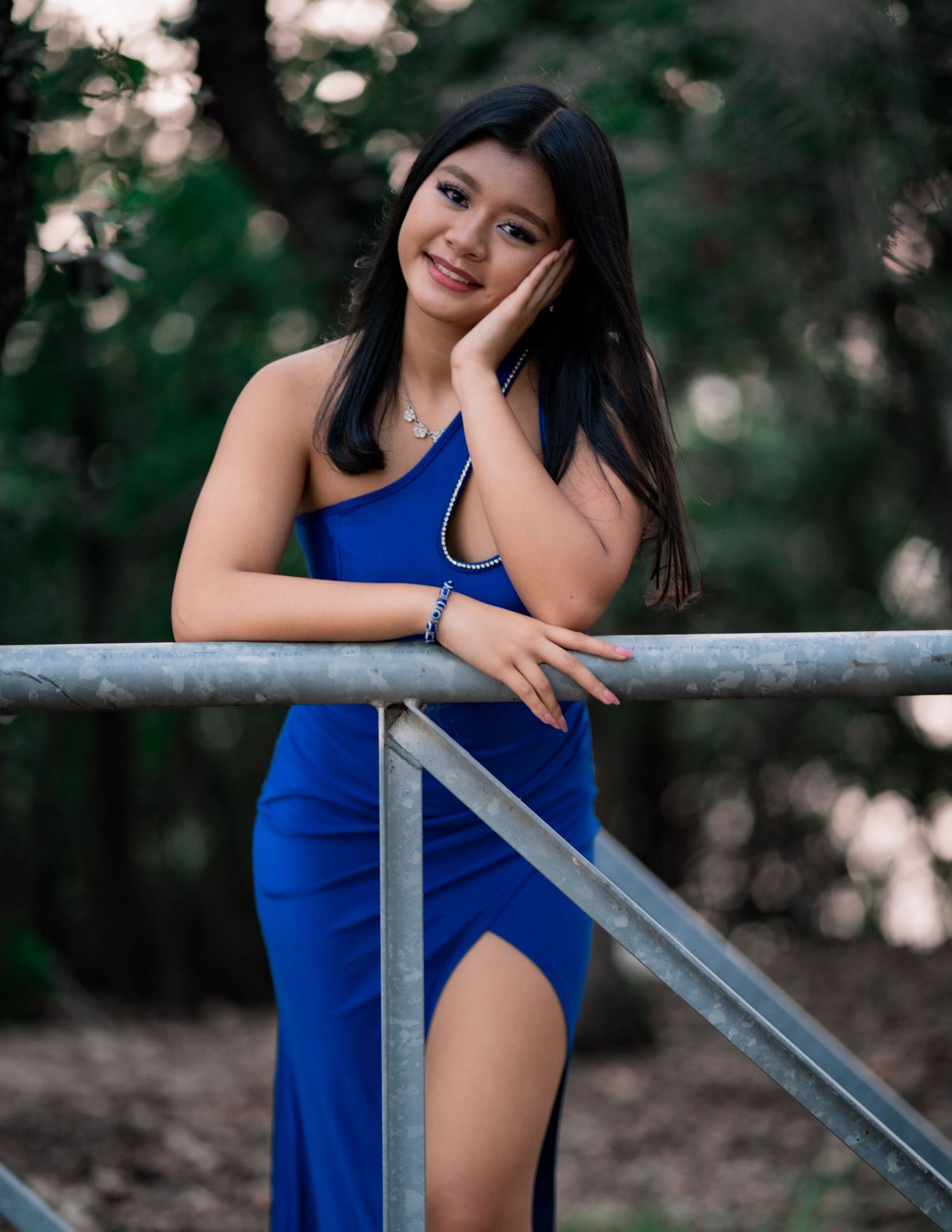 Elegant pose in a royal blue evening gown against a natural outdoor setting.