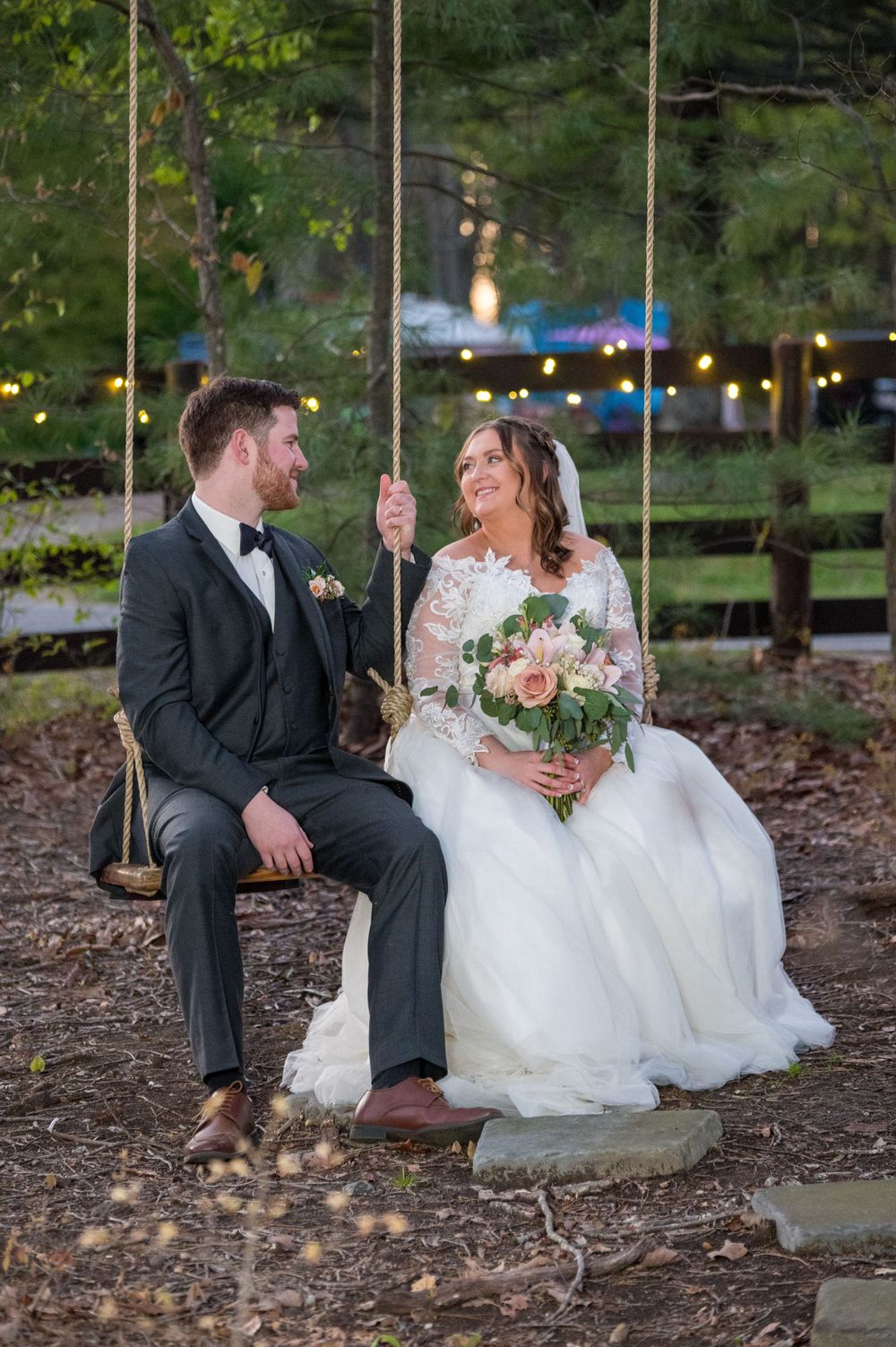A couple sits together on a wooden swing during their wedding celebration.