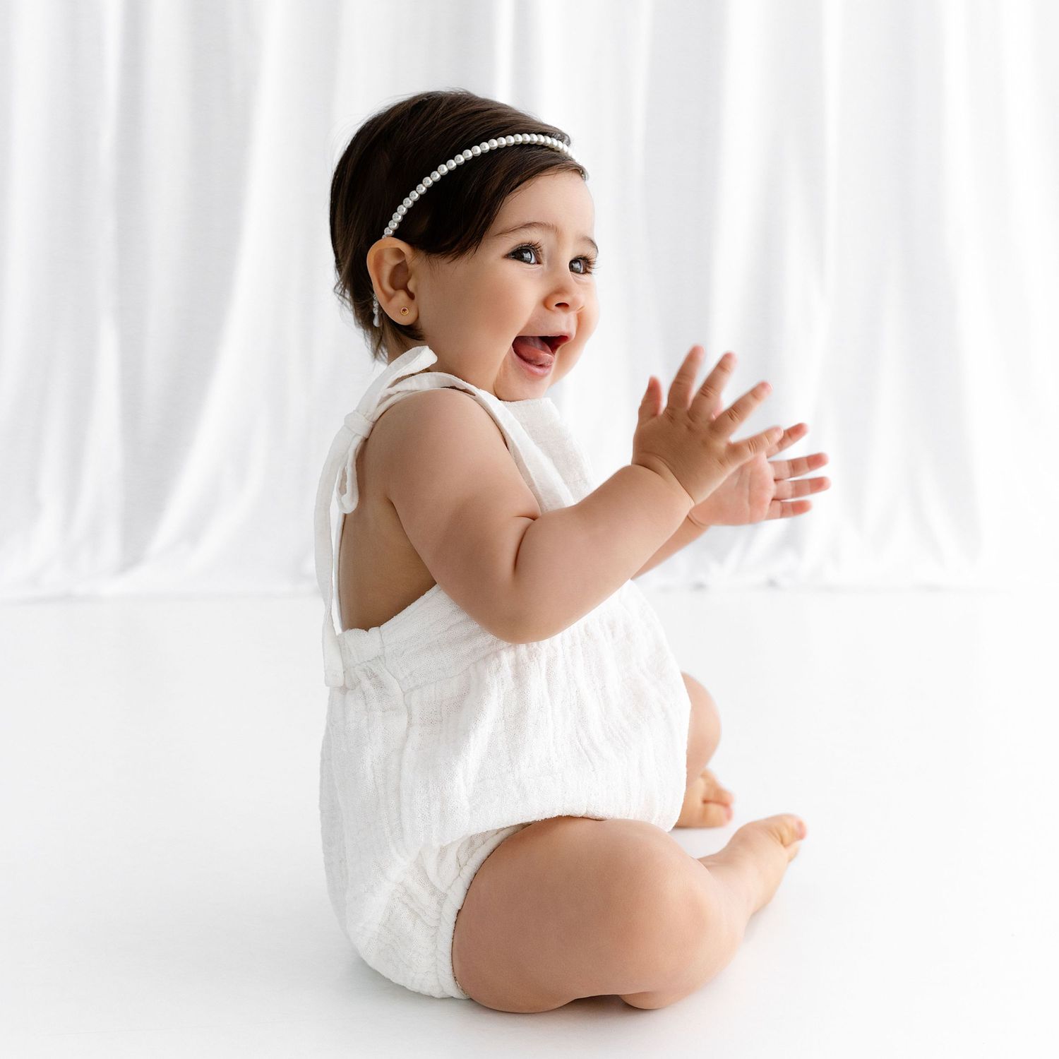 Happy baby in white outfit clapping hands during photo session.