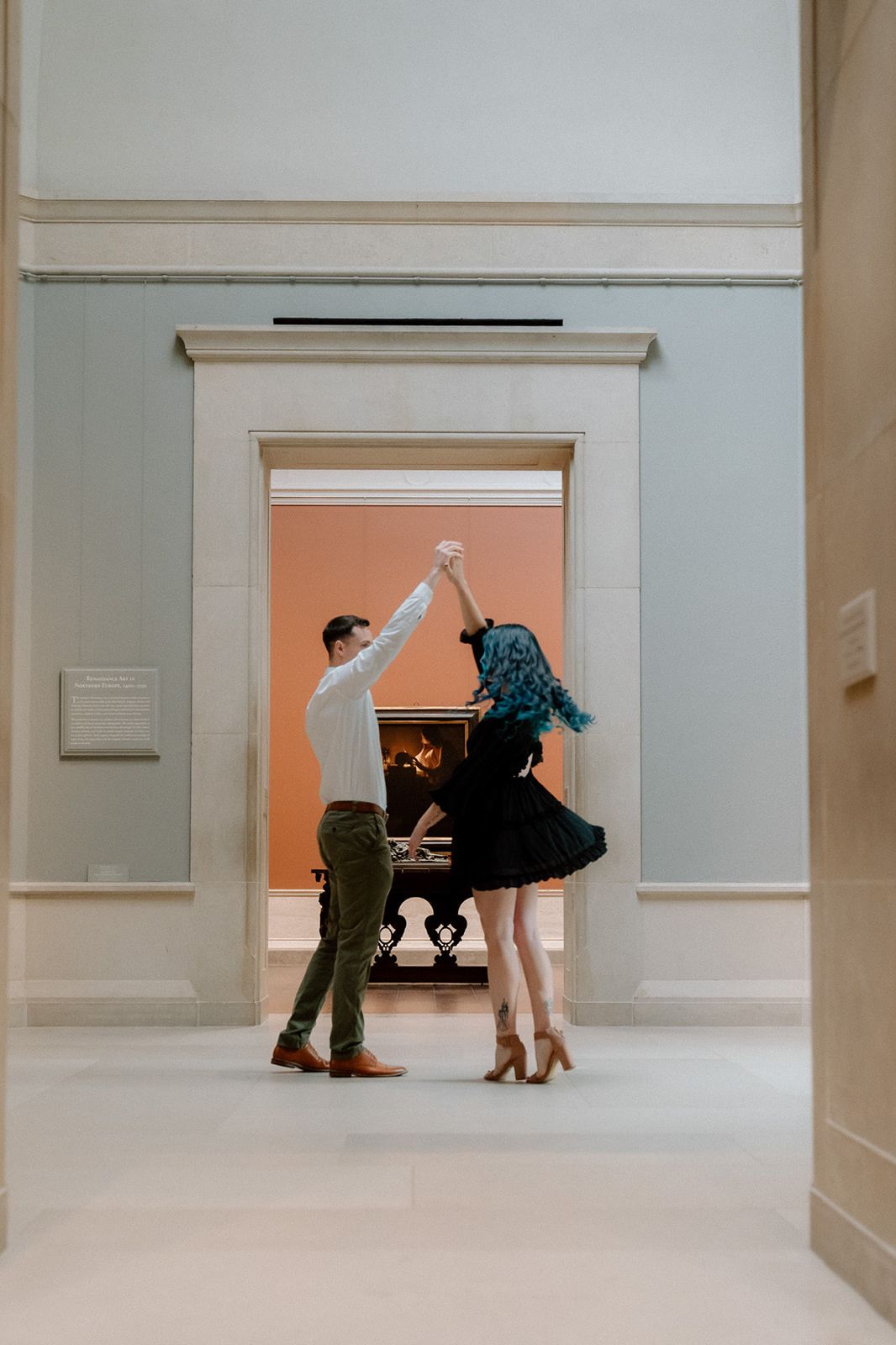 A couple dancing together in an elegant hallway with white walls and a coral-colored doorway at the National Gallery of Art in DC