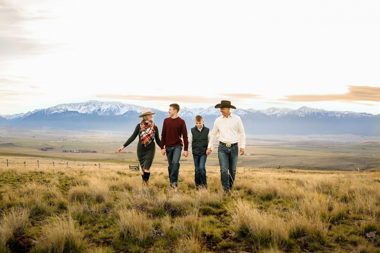 Four people walking through scenic grassland with snow-capped mountains in background. Family Enterprise, Oregon