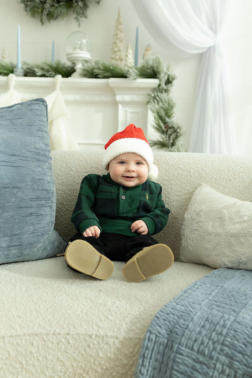 A festive holiday scene with a small figure in a green outfit and Santa hat sitting on a cream colored couch with blue pillows.