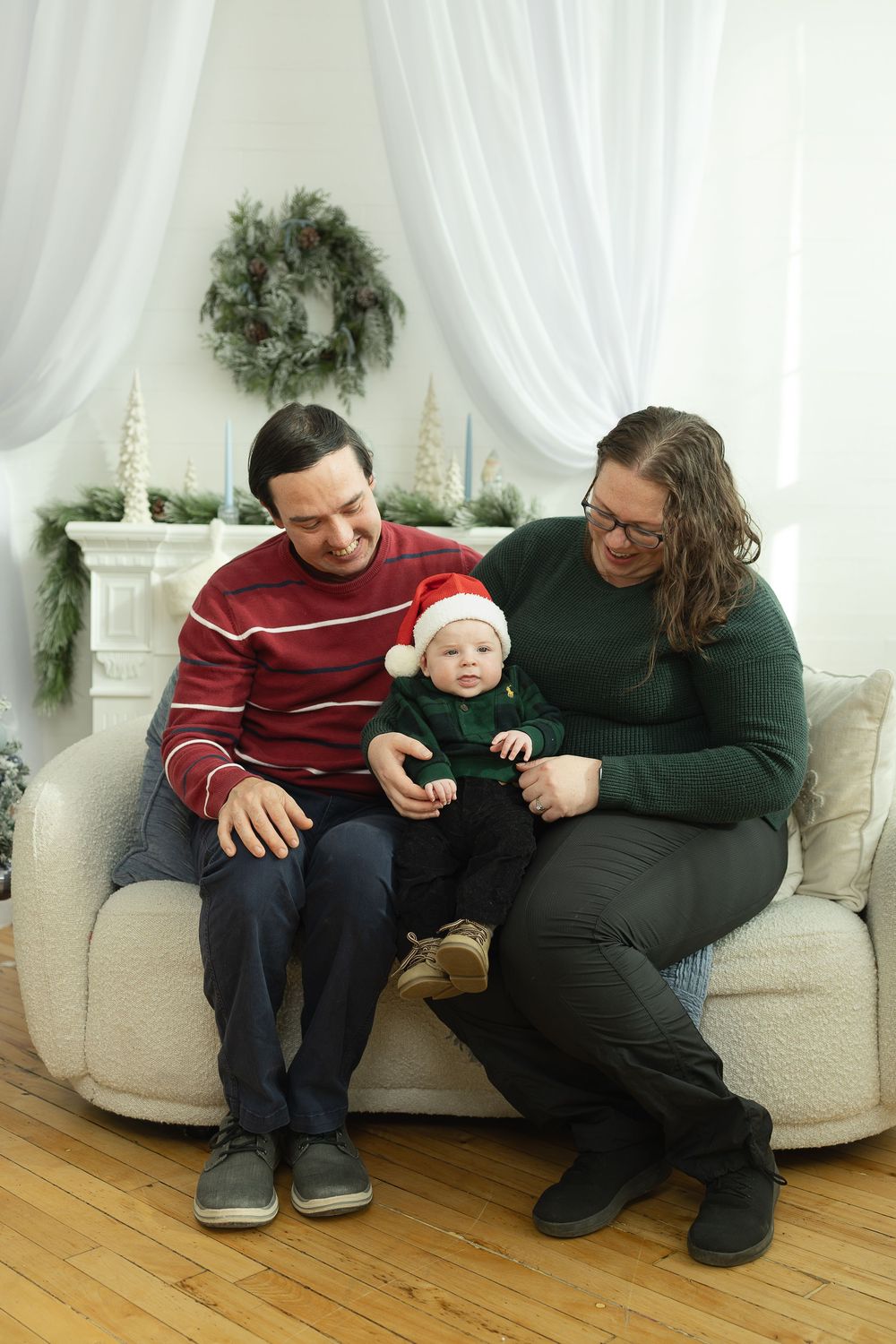 A couple sitting on a beige couch share a laugh while looking at a mobile device together.