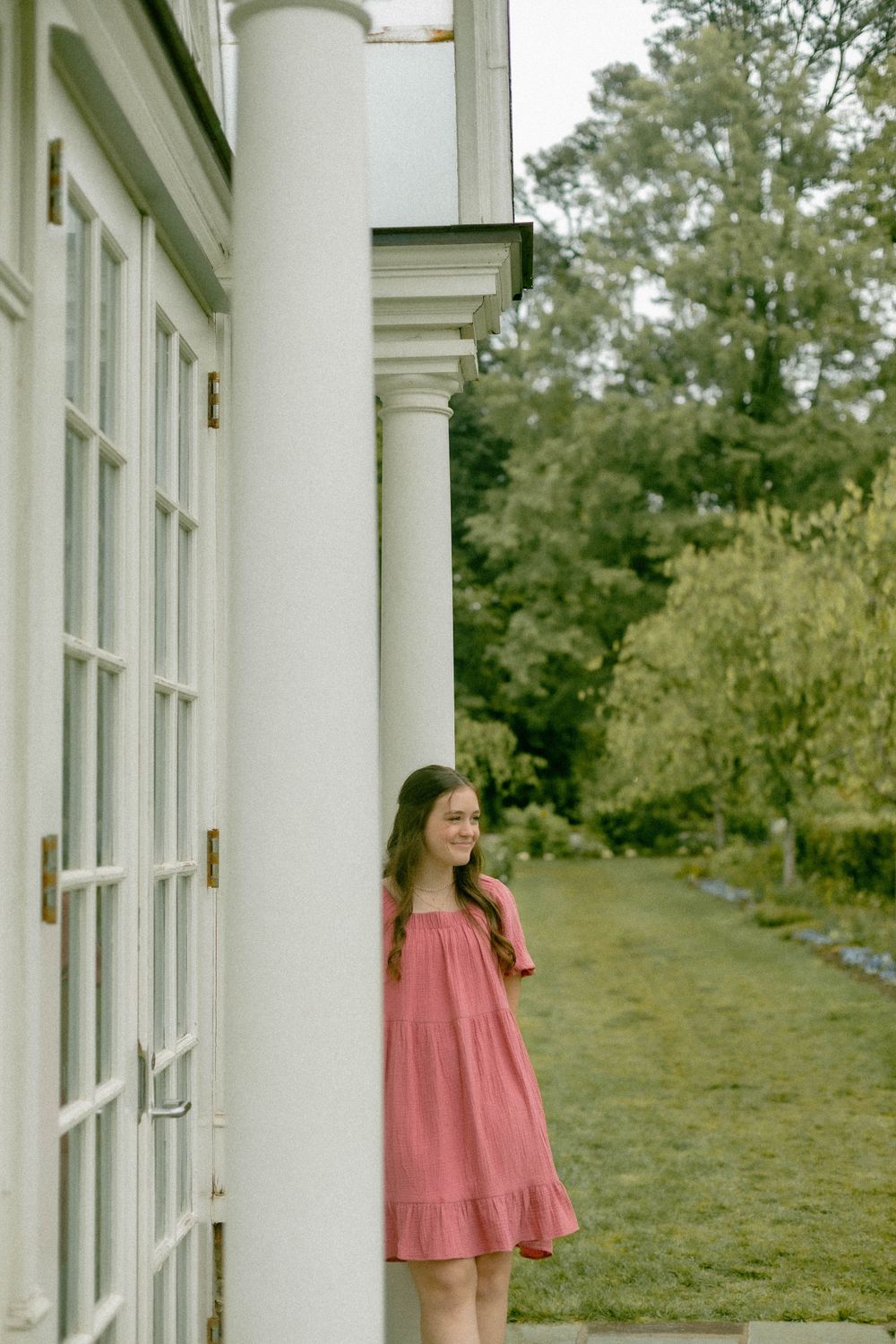Casual portrait beside white columns and windows overlooking a serene garden path.