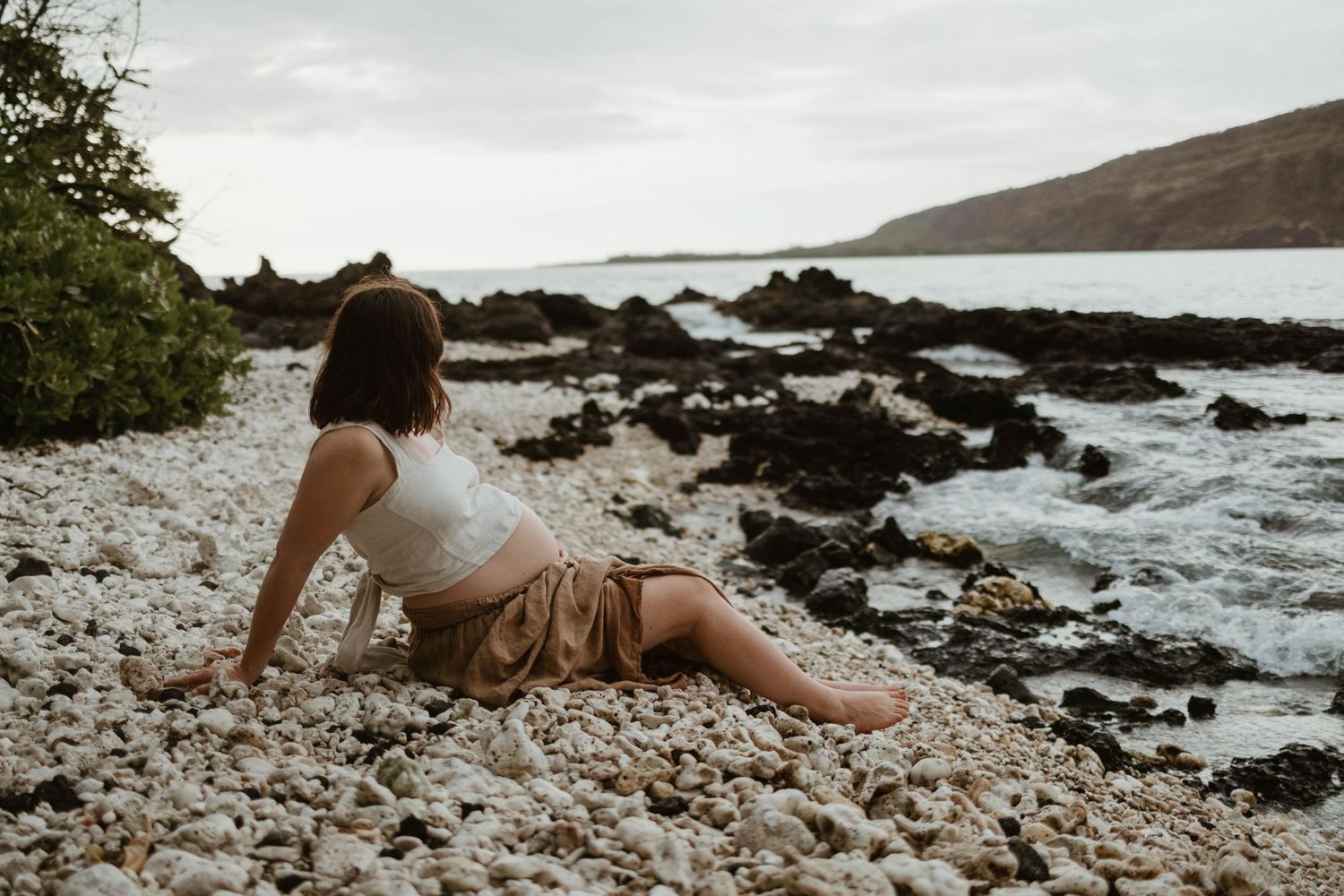 Person lounging on rocky beach beside crashing waves and volcanic rocks in Hawaii.