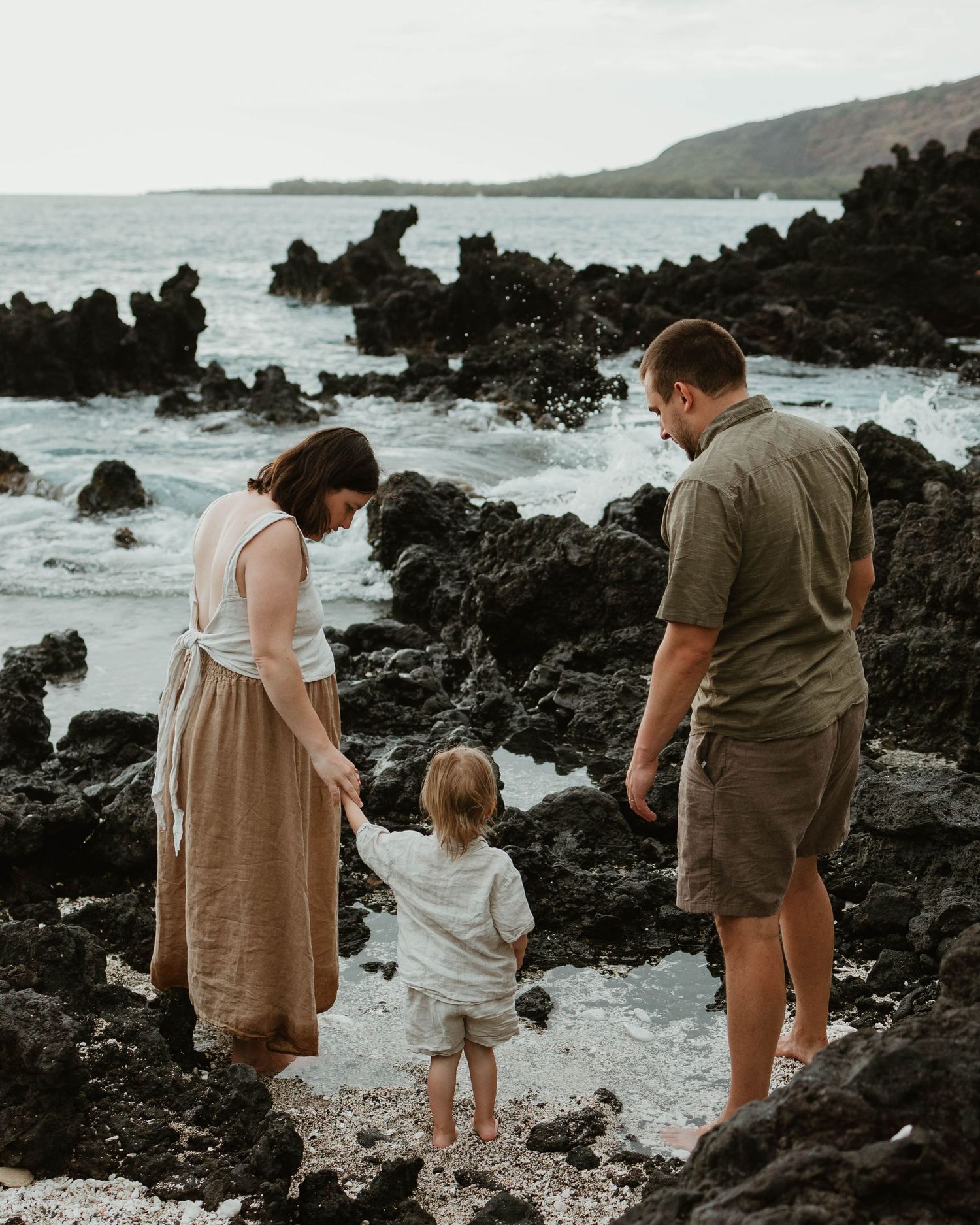 Family exploring rocky volcanic coastline together at sunset in Hawaii.