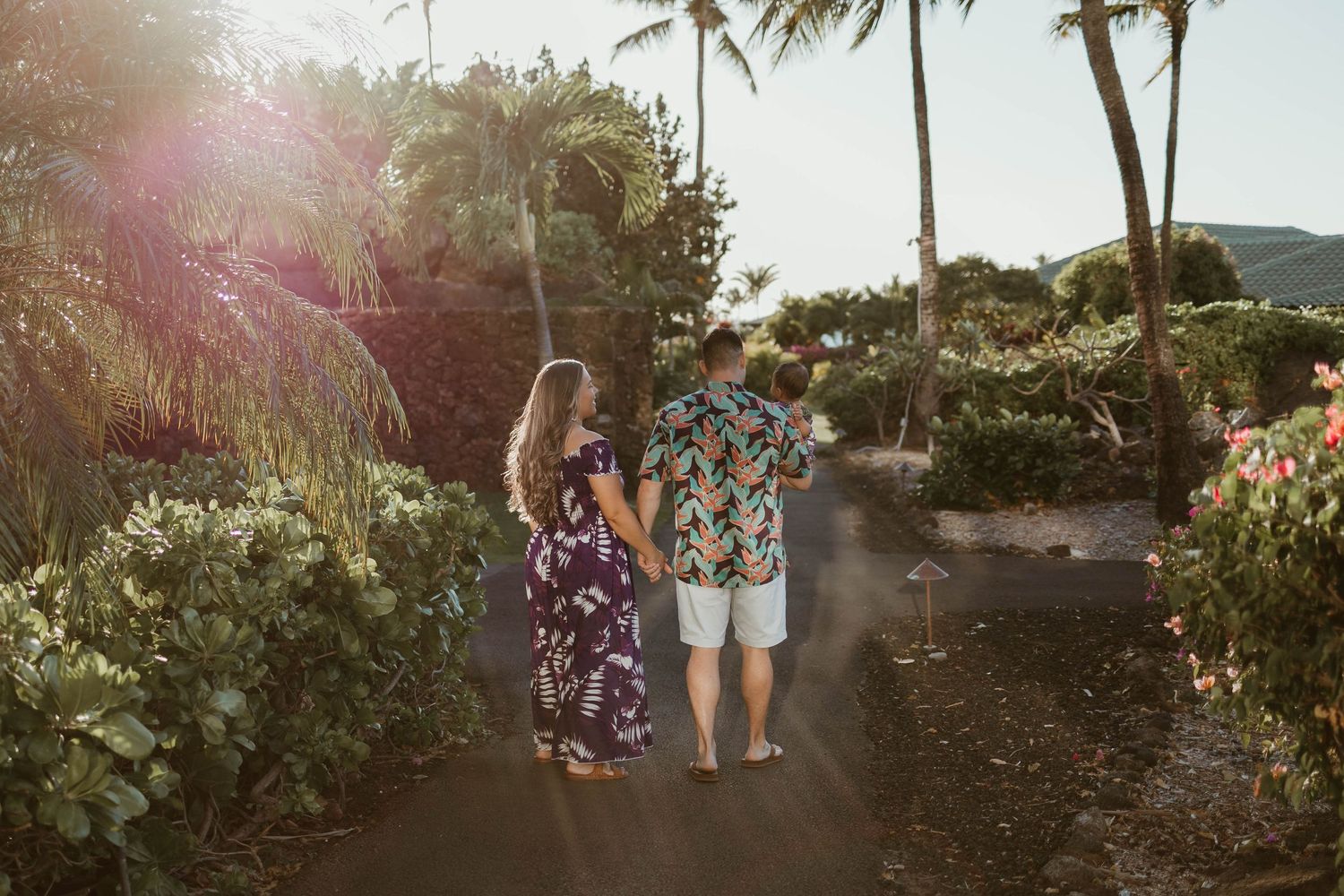 A couple walking down a palm-lined path at sunset with tropical flowers in view.