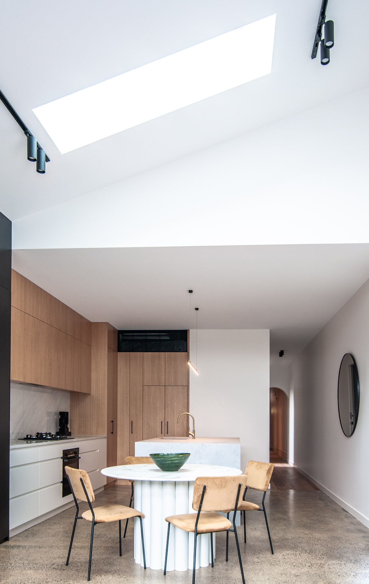 Bright modern kitchen with skylight, wooden cabinetry, and round white dining table.