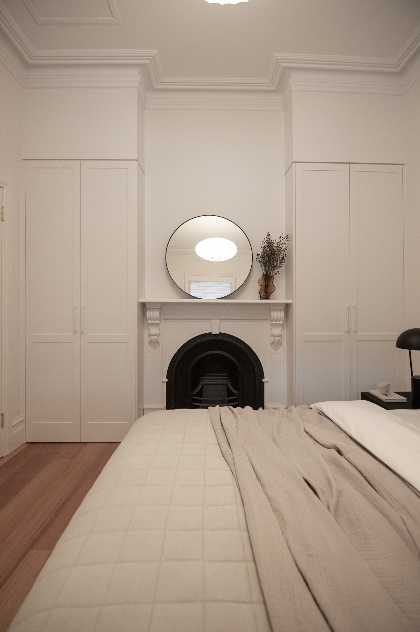 Elegant bedroom interior with white built-in wardrobes, circular mirror, and original fireplace.