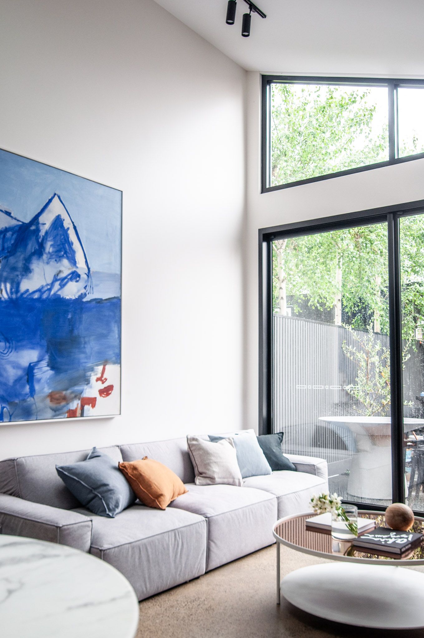 Contemporary living room with mountain artwork, gray sectional sofa and floor-to-ceiling windows.