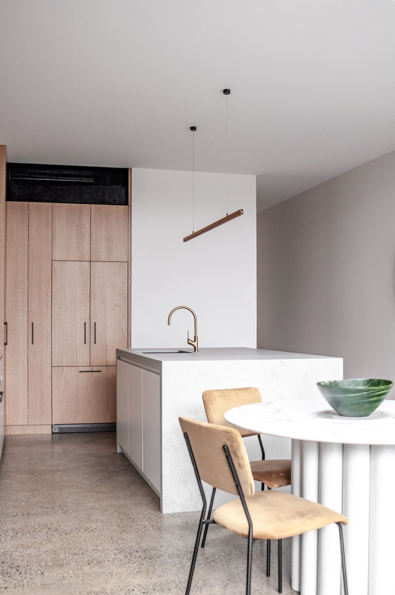 Minimalist kitchen with white island, wooden cabinetry, and pendant lighting above dining area.