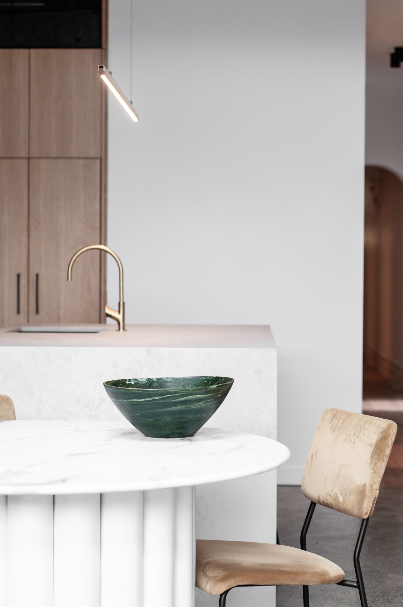 Modern dining area with white fluted island, green ceramic bowl, and wooden chairs.