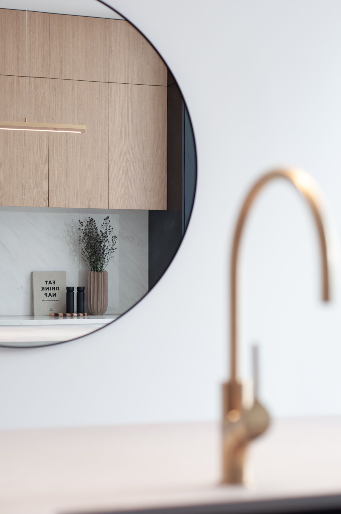 Round mirror reflection showing wooden cabinets with gold faucet in foreground.