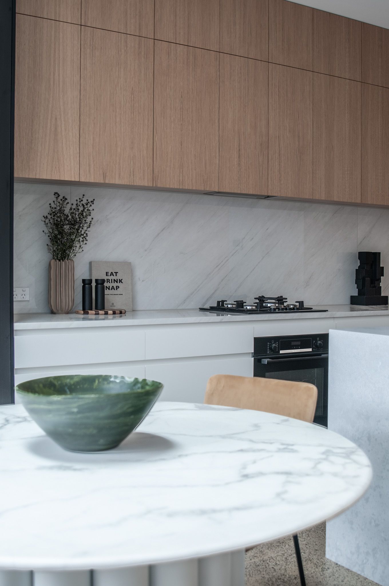 Contemporary kitchen with marble backsplash, wooden cabinets and green ceramic bowl on marble table.