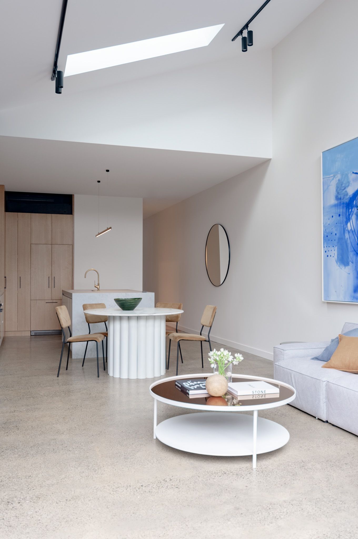 Open concept living space with skylight, white furniture and blue artwork on wall.