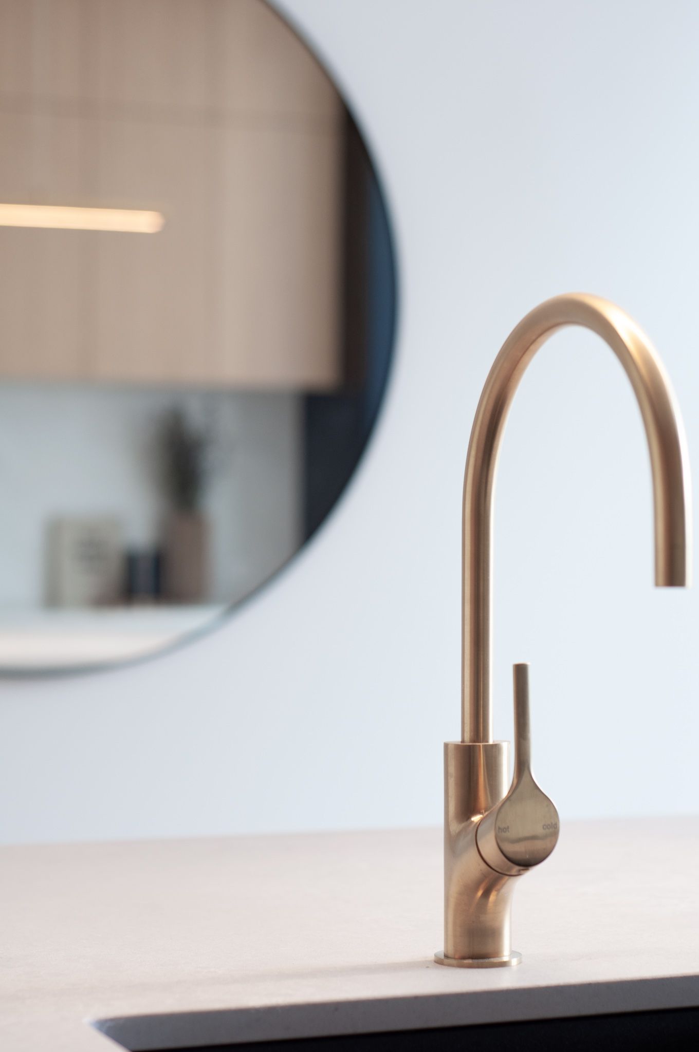 Close-up of gold kitchen faucet with round mirror reflection in background.