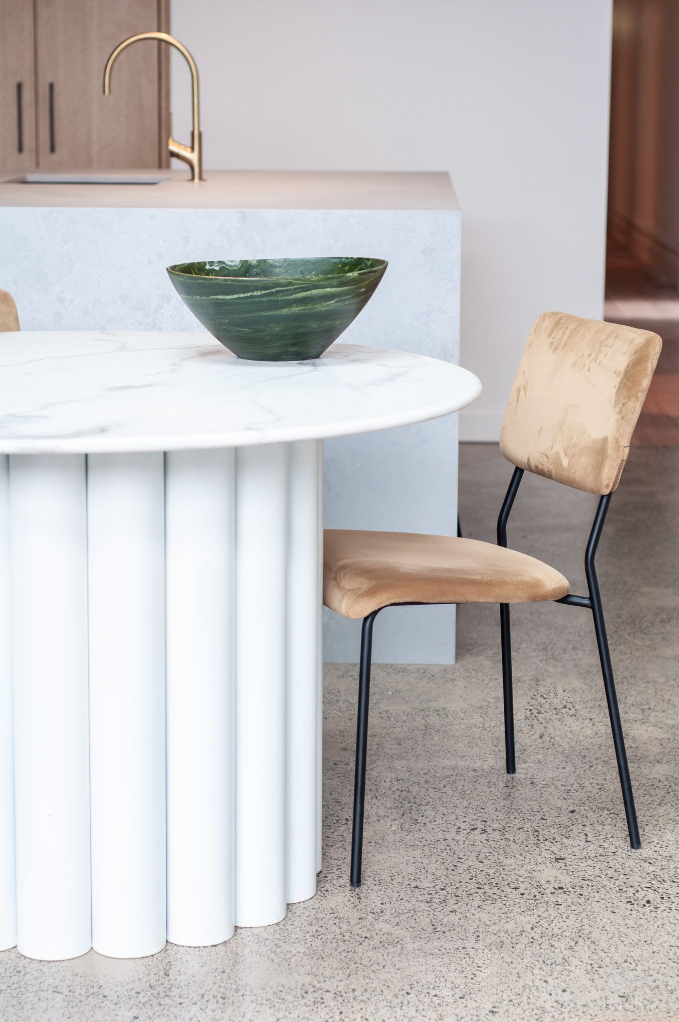 Modern dining area featuring a sculptural white table base, wooden chair, and green ceramic bowl.