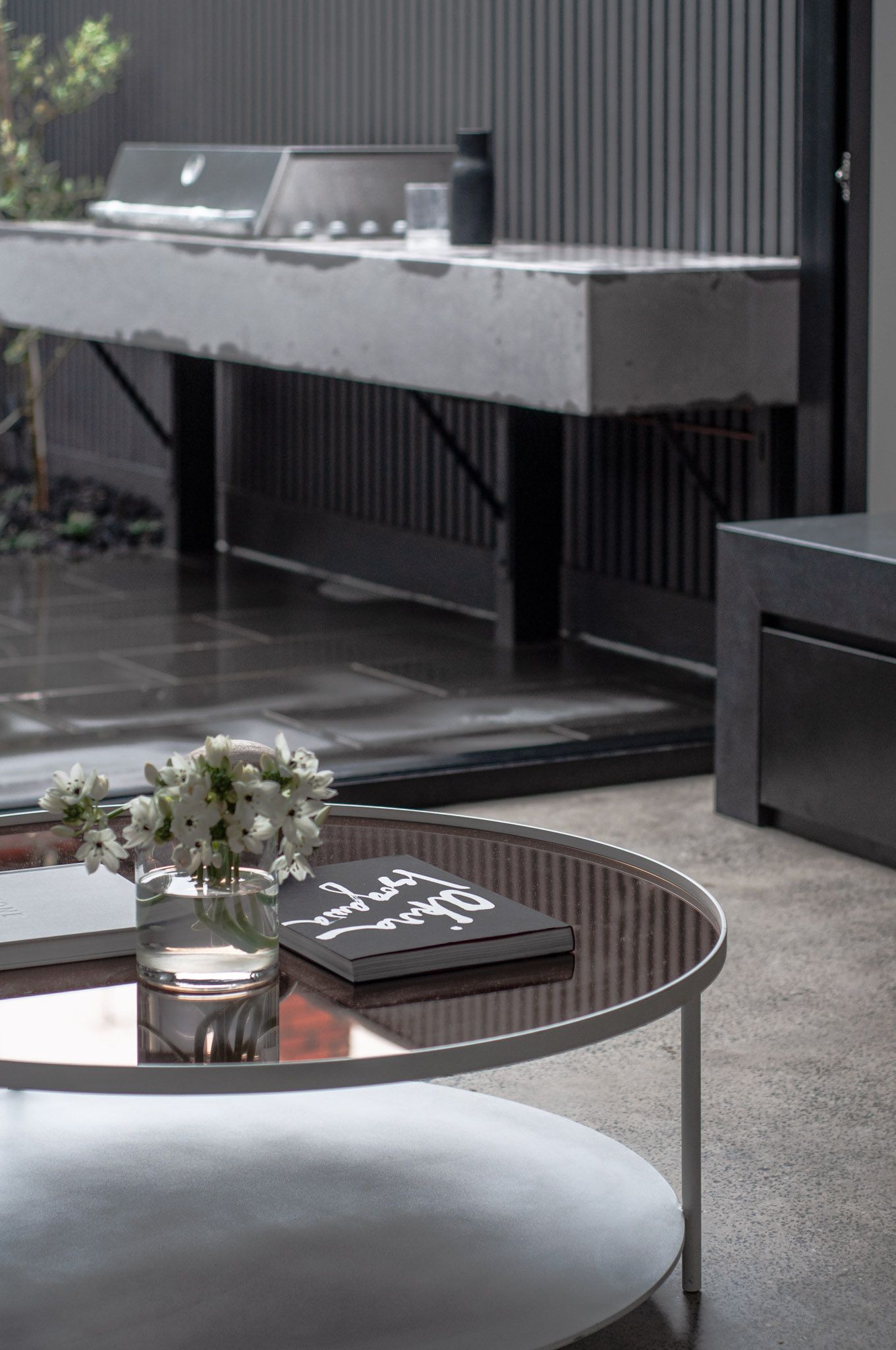 Outdoor entertaining area with concrete bench and round metal coffee table with floral centerpiece.