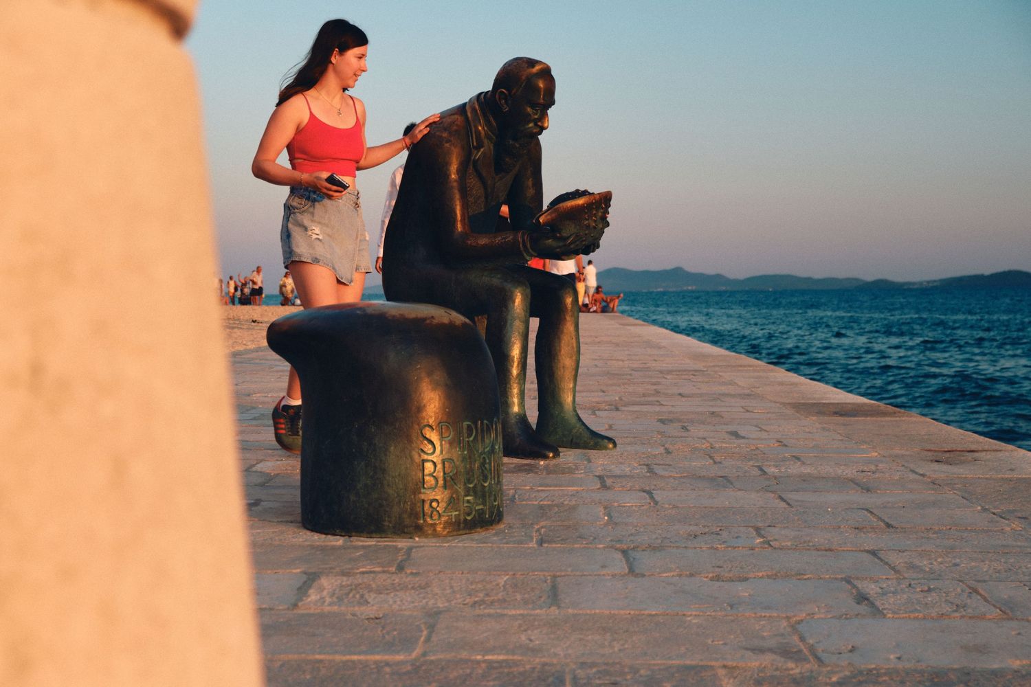 People relaxing on a stone pier by the ocean at sunset.