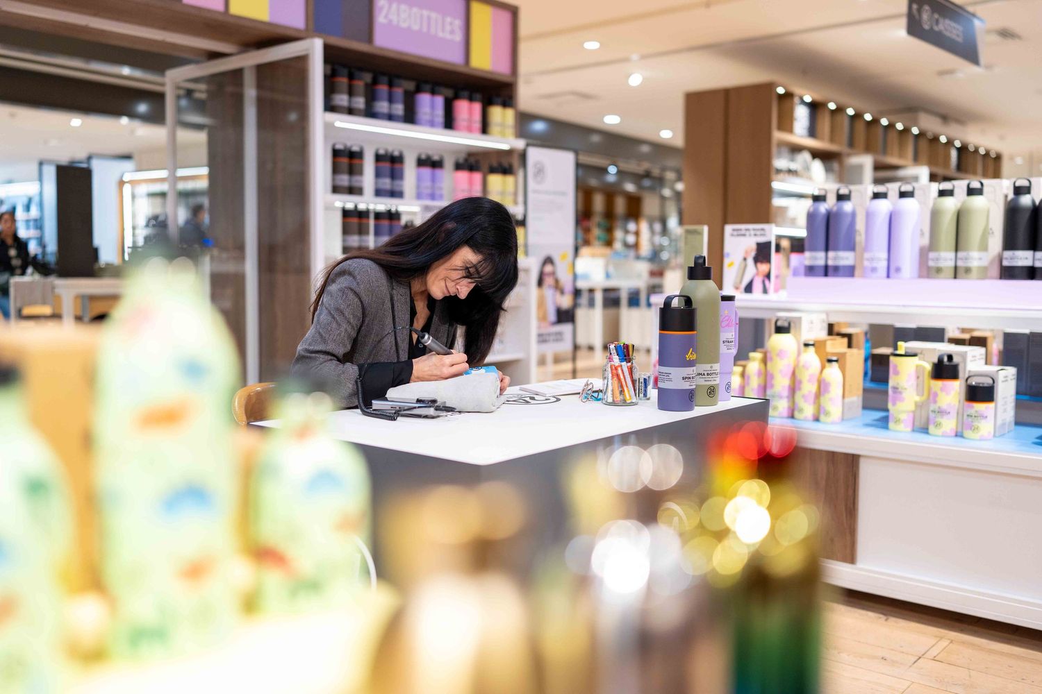 A person works at a beauty counter display in a retail store surrounded by cosmetic products and lighting fixtures.