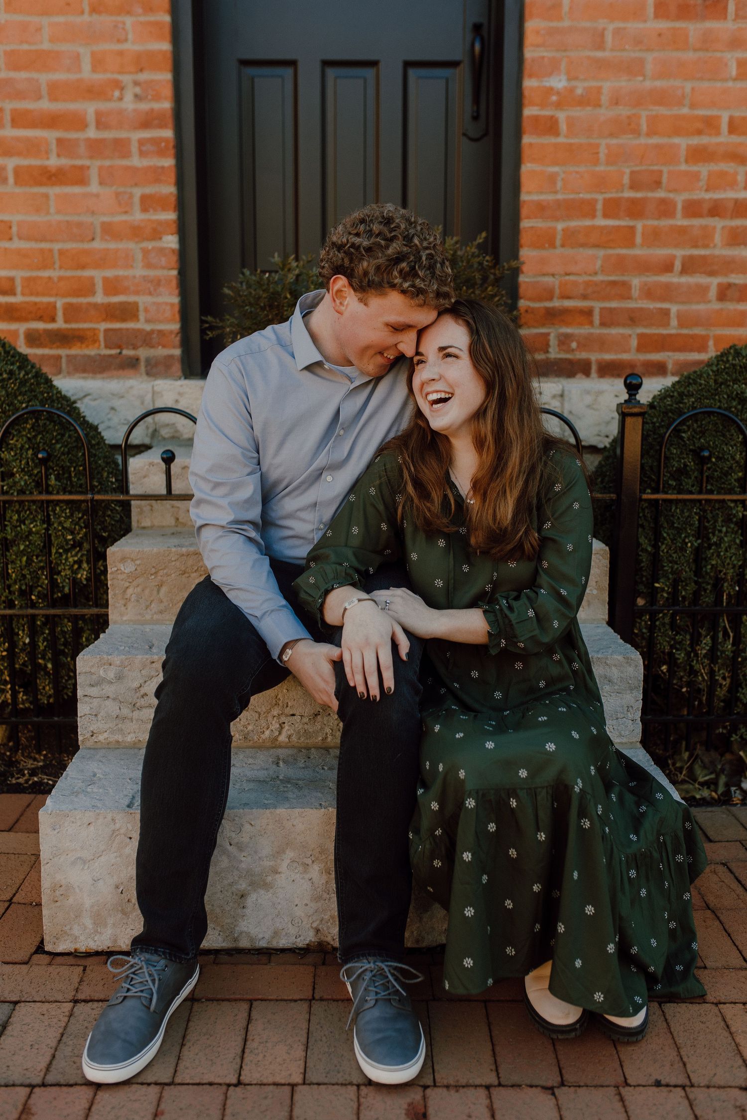 Couple sharing a candid moment on brick steps, wearing casual clothing and smiling.