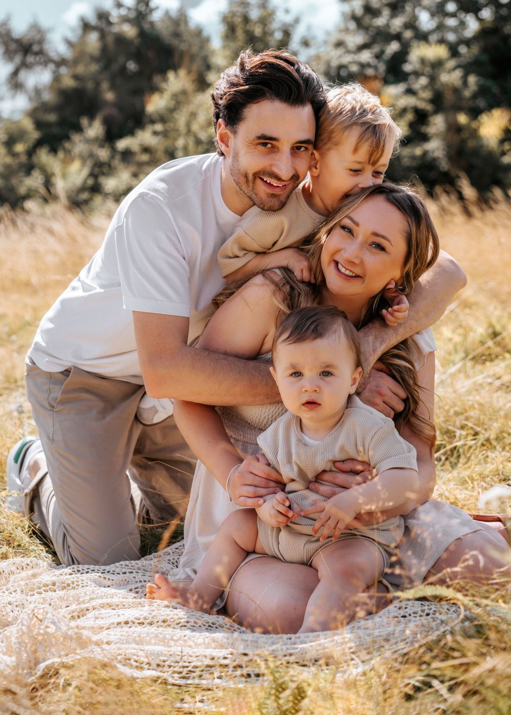 Happy family sitting together on a blanket in a sun-lit meadow during a warm summer day. Family Photoshoot.