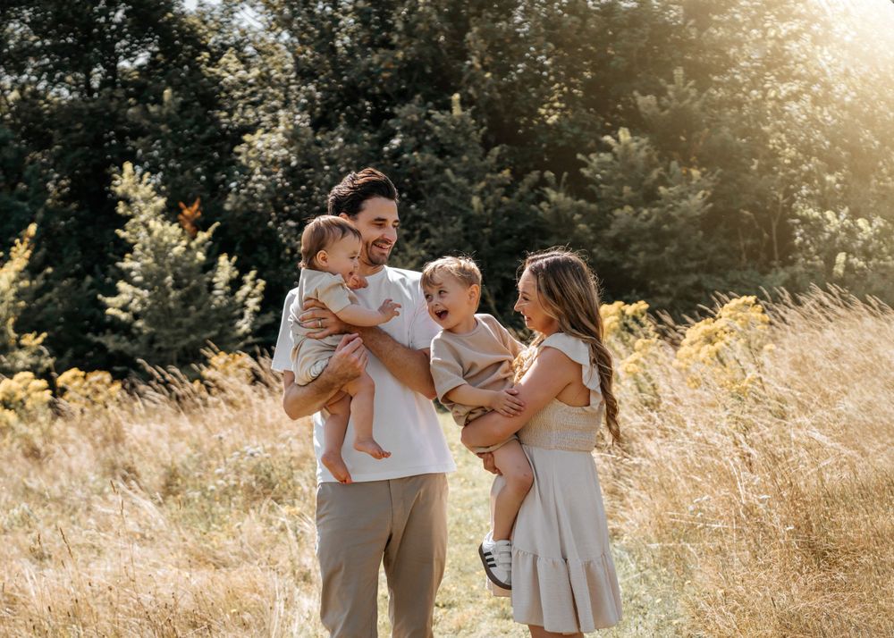 A family shares a joyful moment together in a sunlit meadow with tall golden grass and evergreen trees. Family Photoshoot.