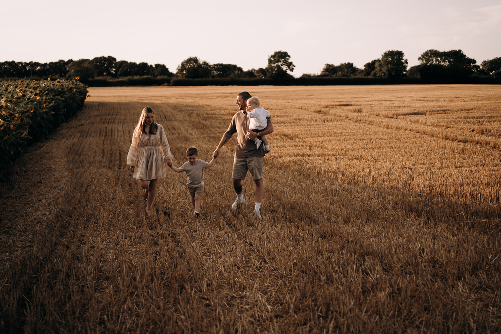 A family walks together at sunset through a golden wheat field along a dirt path in summer. Family Photoshoot.