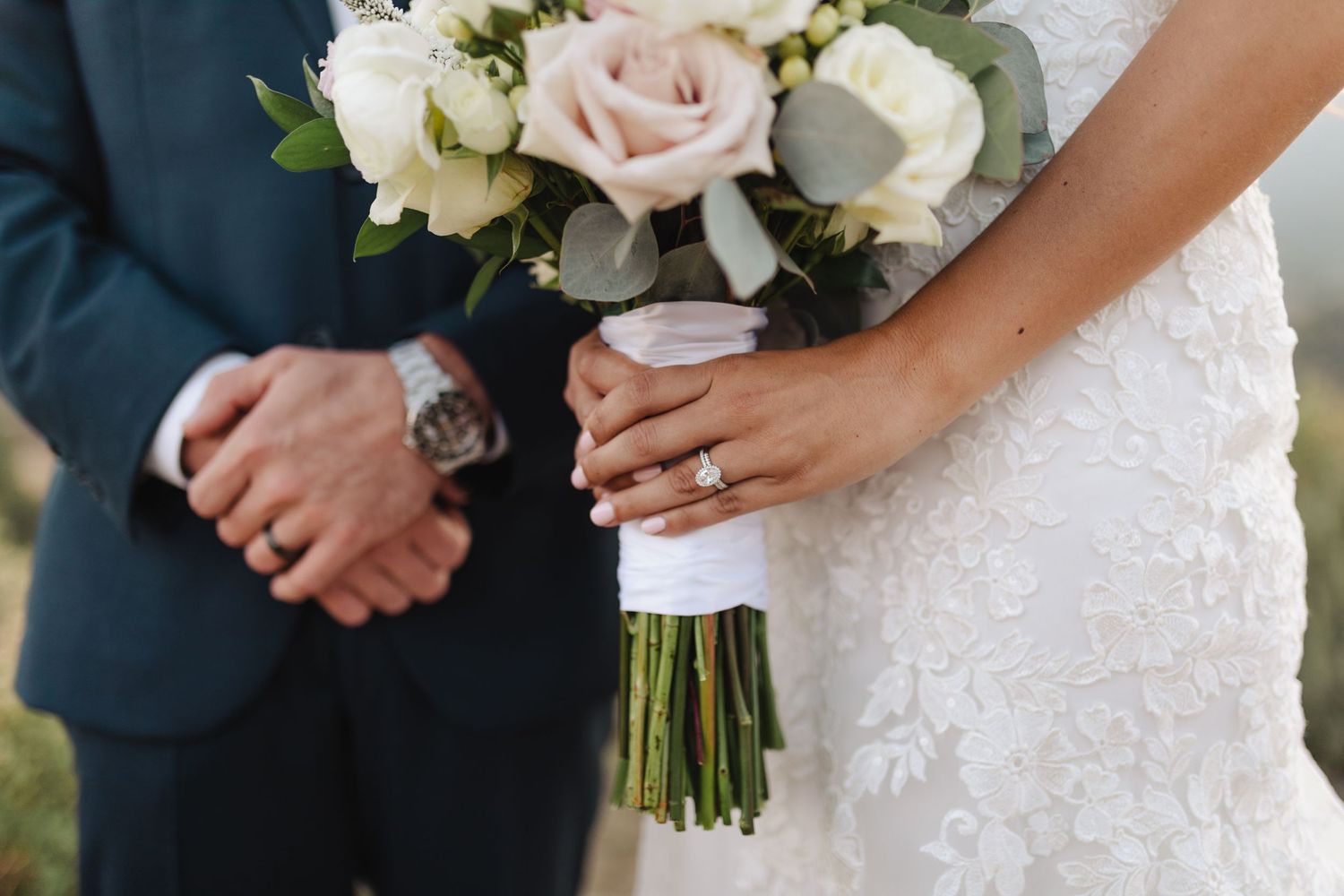 Close-up of hands holding a bridal bouquet with white and blush roses.