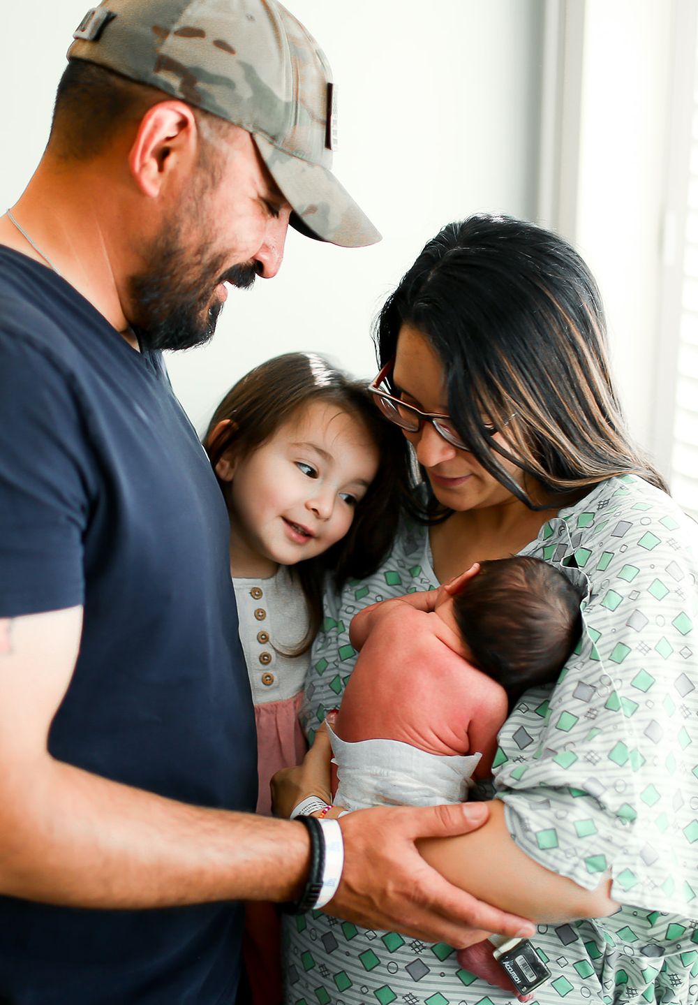 A family shares an intimate moment together while cradling their newborn baby in a bright indoor setting.