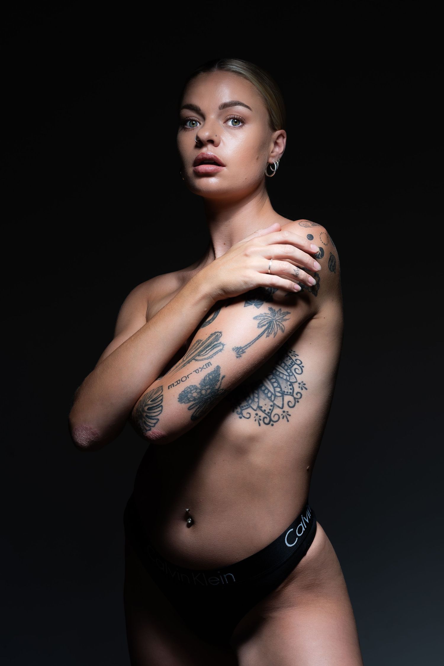 Artistic black and white portrait showing tattooed arm and dramatic lighting against dark background.