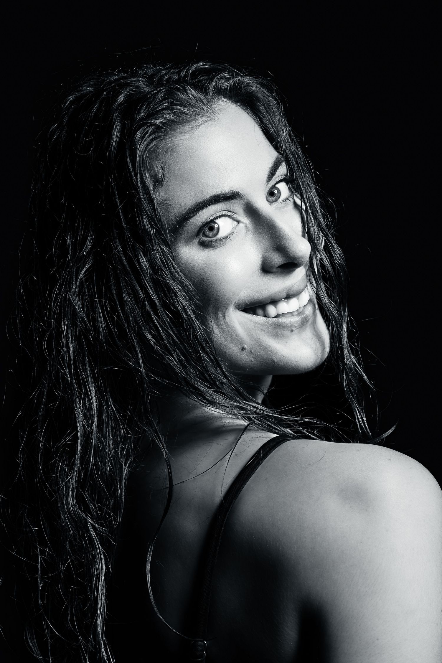 Black and white portrait of a smiling woman with wet hair against a dark background.
