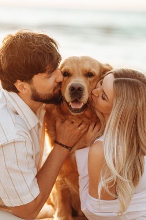Couple sharing affectionate moments with their golden retriever dog at sunset.