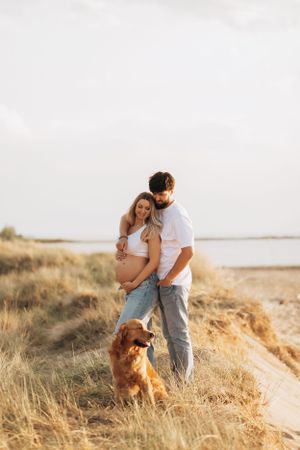Sunset maternity photos with couple and dog in golden field.