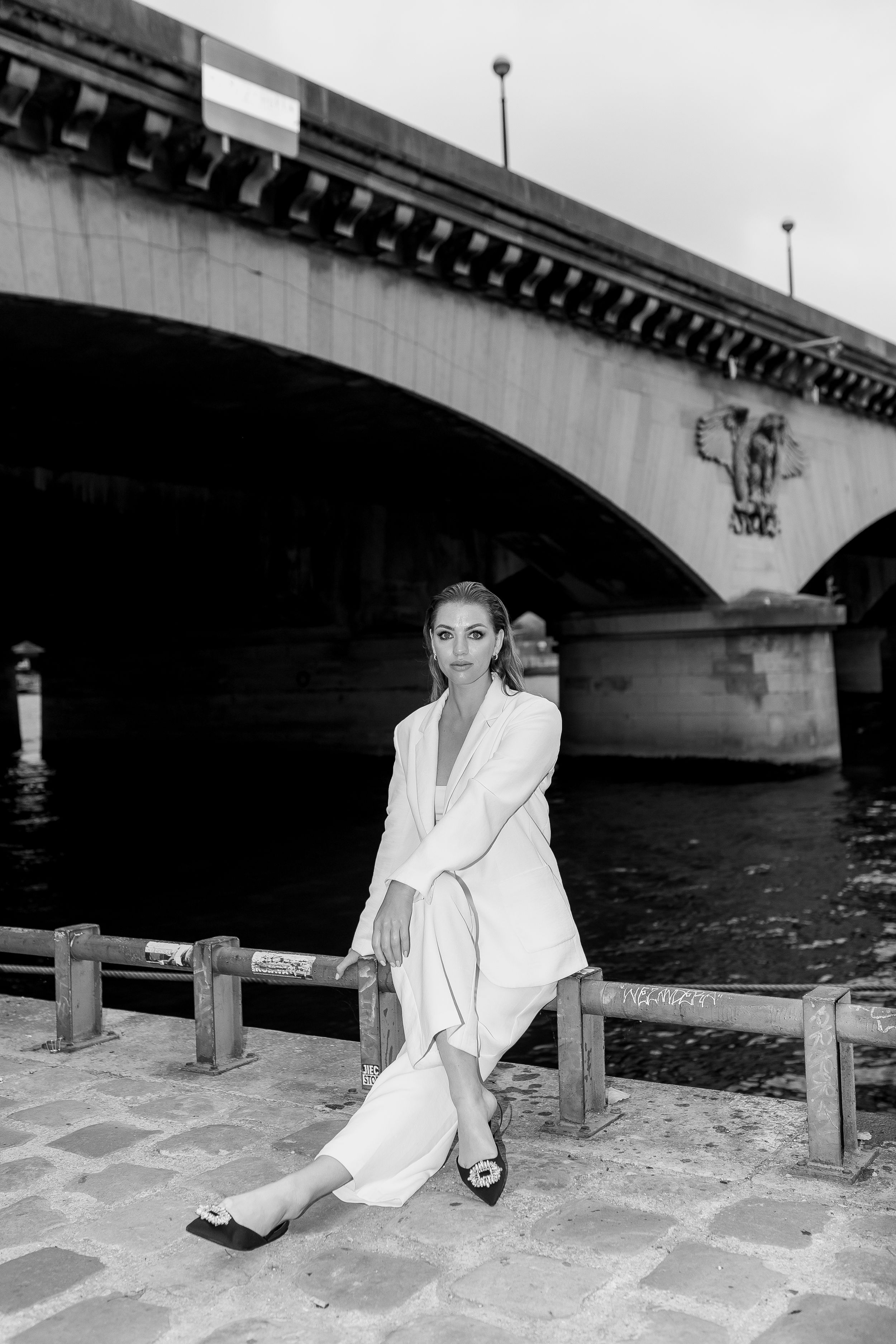 Black and white photo series of someone in white clothing posing by a bridge.