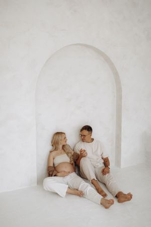 Intimate maternity photo of couple sitting in white arched alcove.
