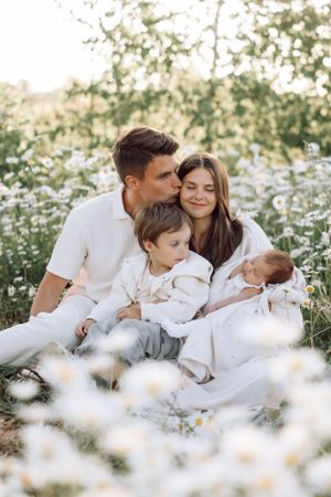 Family lying together in blooming daisy field during spring photoshoot.