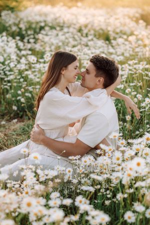 Romantic couple photoshoot in field of blooming daisies during golden hour.