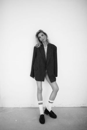 Fashion editorial shot of model in oversized blazer and knee socks against white background.