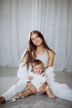 Candid lifestyle photos of parent and baby playing on white floor with curtain backdrop.