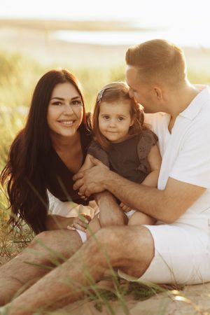 Family sitting together in golden field during sunset photo session.